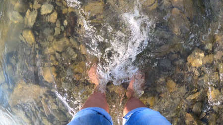 Girl stands barefoot on stones shallow riverの写真素材