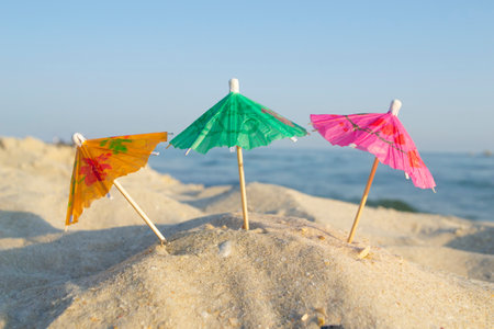 Three small paper cocktail umbrellas stand in sand on sandy beach close-up.の写真素材