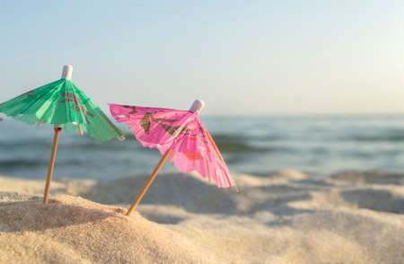 Three small paper cocktail umbrellas stand in sand on sandy beach close-up.の写真素材