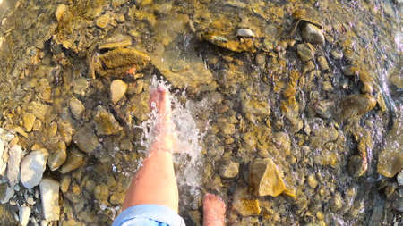 Girl bare foot water sprays on stones of shallow river close-up, sunny summerの写真素材