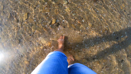 Girl walks barefoot on a sandy bottom with stones of the sea shoreの写真素材