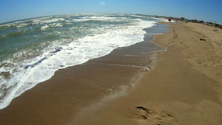 Sea wave with white foam rolls over sandy shore of beach. Top view.の写真素材