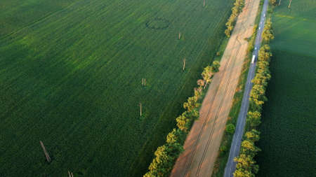Drone flying over road between green agricultural fields during dawn sunset.の写真素材