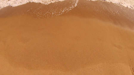 Sea wave with white foam rolls over sandy shore of beach. Top view.の写真素材