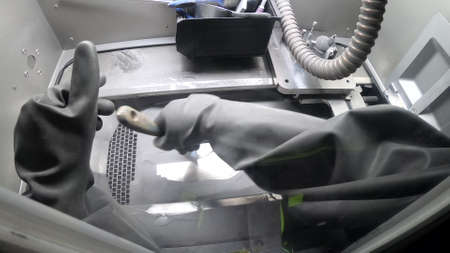 Male worker in rubber glove cleans printing platform inside 3d printer for metalの写真素材