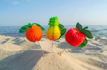 Three paper fruits on stick stand on sandy beach near sea on sunny summer dayの写真素材
