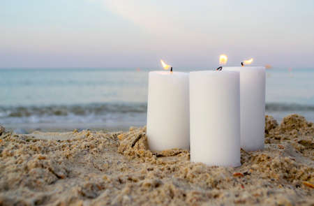 Three large white paraffin candles burn on sand beach background seaの写真素材