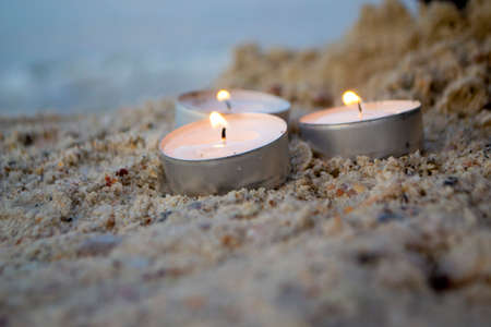 Three small burning candles on sand beach on background of blurry sea wavesの写真素材