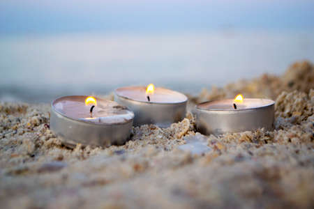 Three small burning candles on sand beach on background of blurry sea wavesの写真素材