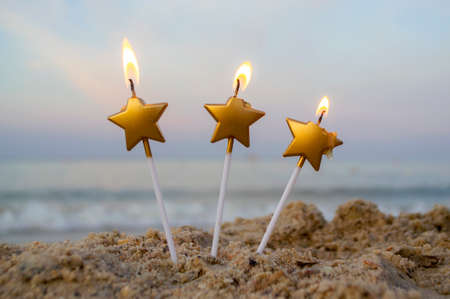 Three candles form of star burn in sand on beach on backgroundの写真素材