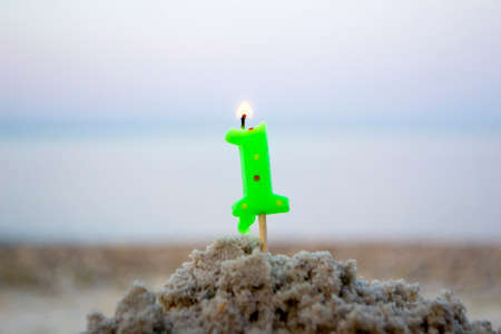 Candle number one on stick inserted into sand and burns. Lighted candleの写真素材