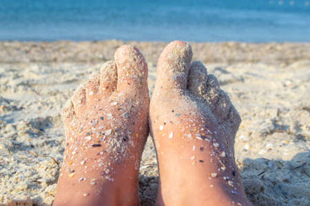 Two bare feet of caucasian woman soiled in sand with shell rock on sandy seaの写真素材