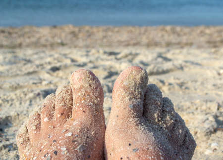 Two bare feet of caucasian woman soiled in sand with shell rock on sandy seaの写真素材