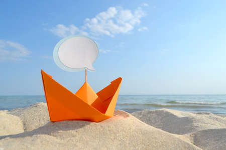 Orange Paper Boat on Sandy Seashore Close-up Small Boat from Paper on Backgroundの写真素材