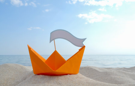 Orange Paper Boat on Sandy Seashore Close-up Small Boat from Paper on Backgroundの写真素材