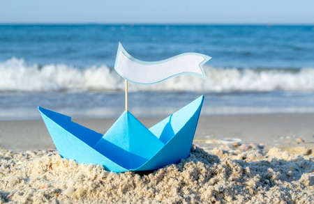 Blue paper boat on a sandy beach near the sea on a sunny summer dayの写真素材