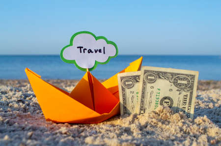 Two paper one dollars bills half buried in sand and orange paper boatの写真素材