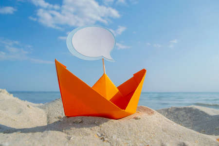 Orange Paper Boat on Sandy Seashore Close-up Small Boat from Paper on Backgroundの写真素材