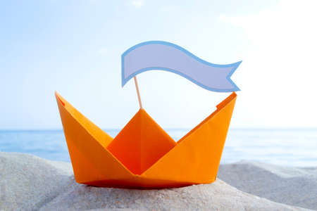 Orange Paper Boat on Sandy Seashore Close-up Small Boat from Paper on Backgroundの写真素材