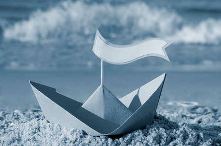 Blue paper boat on a sandy beach near the sea on a sunny summer dayの写真素材