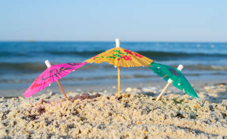 Three small paper cocktail umbrellas stand in sand on sandy beach close-upの写真素材
