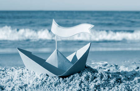 Blue paper boat on a sandy beach near the sea on a sunny summer day.の写真素材