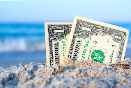 Two one dollar bills half buried in sand on sandy seashore close-up.の写真素材
