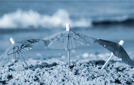 Three small paper cocktail umbrellas stand in sand on sandy beach close-upの写真素材