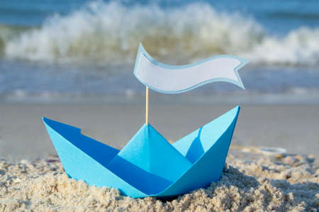 Blue paper boat on a sandy beach near the sea on a sunny summer day.の写真素材