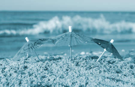 Three small paper cocktail umbrellas stand in sand on sandy beach close-upの写真素材