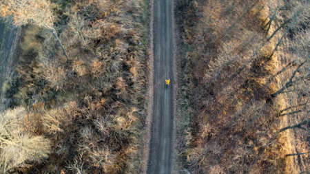 Aerial drone view man in yellow jacket rides bicycle on black dirt roadの写真素材