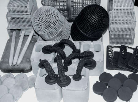 Many different models printed on 3D printer. Gray and black objects printed on 3D printer made of plastic close-up. Lots of 3D printed models. Prototypes of various shapes made by 3d printer on table.の写真素材