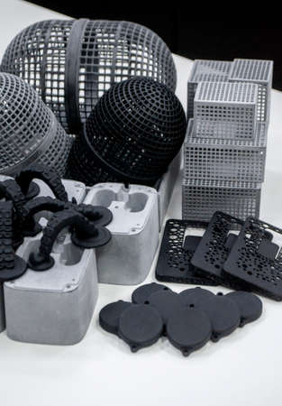 Many different models printed on 3D printer. Gray and black objects printed on 3D printer made of plastic close-up. Lots of 3D printed models. Prototypes of various shapes made by 3d printer on table.の写真素材