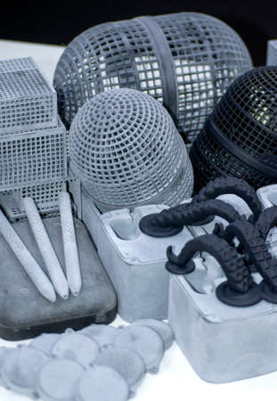 Many different models printed on 3D printer. Gray and black objects printed on 3D printer made of plastic close-up. Lots of 3D printed models. Prototypes of various shapes made by 3d printer on table.の写真素材