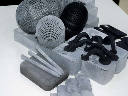 Many different models printed on 3D printer. Gray and black objects printed on 3D printer made of plastic close-up. Lots of 3D printed models. Prototypes of various shapes made by 3d printer on table.の写真素材