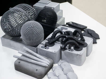 Many different models printed on 3D printer. Gray and black objects printed on 3D printer made of plastic close-up. Lots of 3D printed models. Prototypes of various shapes made by 3d printer on table.の写真素材