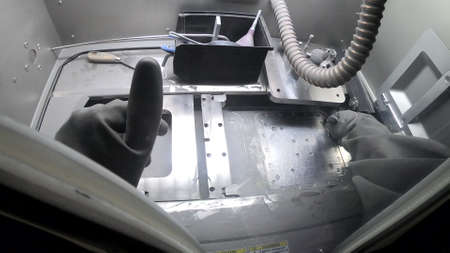 Worker in isolated black rubber gloves cleans brush printing platform inside of 3d printer for metal. Person in gloves cleans metal powder inside industrial machine. Laser sintering machine for metal.の写真素材