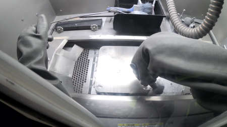 Worker in isolated black rubber gloves cleans brush printing platform inside of 3d printer for metal. Person in gloves cleans metal powder inside industrial machine. Laser sintering machine for metal.の写真素材