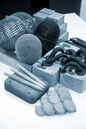 Many different models printed on 3D printer. Gray and black objects printed on 3D printer made of plastic close-up. Lots of 3D printed models. Prototypes of various shapes made by 3d printer on table.の写真素材