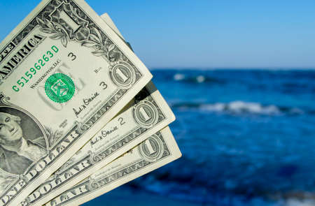 Person holds in his hand three dollar bills on the background of the waves of the blue sea. Concept money finance business tourism travel, money spending, cash expenses. Money cash expenses businessの写真素材