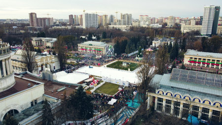 Kiev, Ukraine, January 2, 2022:-Aerial panoramic view cityscape urban park outdoor ice skating rink, many people, high-rise buildings. Cleaning machine cleans ice rink. Public park. New Year Christmasのeditorial素材