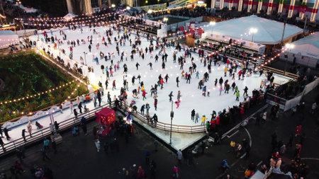 Kiev, Ukraine, January 2, 2022:-Beautiful urban landscape. Many people skating on open-air ice rink with illumination and garlands on winter evening in public city park. Aerial Drone View backgroundのeditorial素材