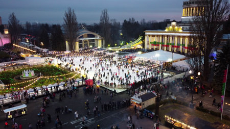 Kiev, Ukraine, January 2, 2022:-Beautiful urban landscape. Many people skating on open-air ice rink with illumination and garlands on winter evening in public city park. Aerial Drone View backgroundのeditorial素材