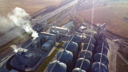 Aerial Drone View Flight Over complex of grain elevator buildings. Metal Round Silos and Metal Barrels for Grain Storage. Drying Storage Harvest. Elevator Tanks and Grain-drying complex. Large Granaryの写真素材