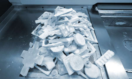 Objects and models printed on industrial 3D printer from white plastic powder close-up in...