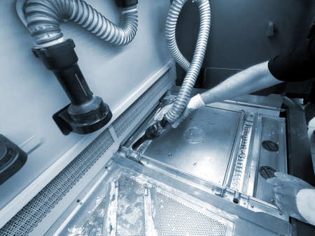A male worker cleans the surface of an industrial 3D printer from white powder with a vacuum cleaner...