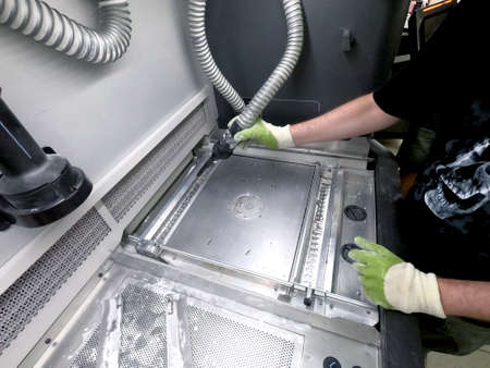 A male worker cleans the surface of an industrial 3D printer from white powder with a vacuum cleaner close-up. Multi Jet Fusion MJF 3D printing. The working processの写真素材