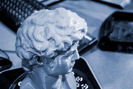 Gray human head on 3d printed close-up. An object prototype of a human head with hair printed by a 3D printer stands on a table. New modern additive 3D printing technology. Fused deposition modelingの写真素材