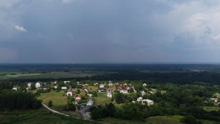 Landscape rural houses, forest, field, rain and dark storm clouds. Houses of the village, lit by sun...