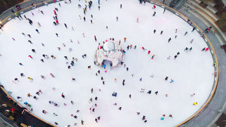 Many people are skating on a white outdoor ice rink in the city on winter day. People skating on the...